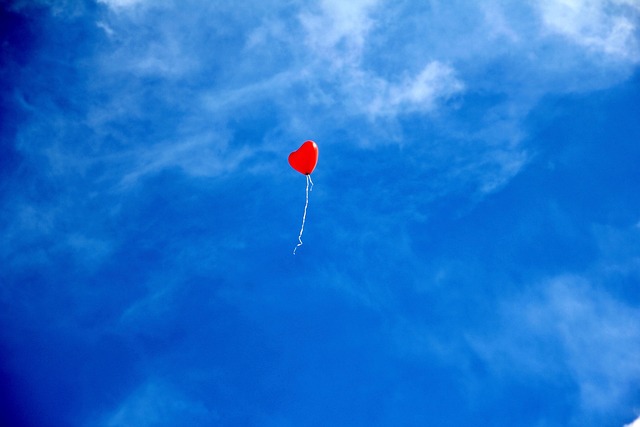 ein roter Ballon in Herzform fliegt durch einen blauen Himmel